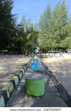 the seats are made of pipes and are colored yellow and green against a backdrop of pine trees and clean beach sand Royalty-Free Stock Photo #2287049897
