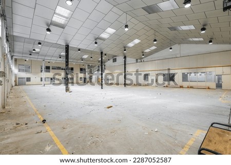 Large garage building with metal beams and ceiling with windows and doors prepared for renovation into a factory or warehouse. Concept of urban surface parking indoors
