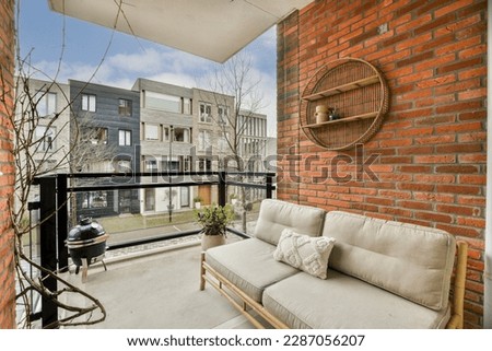 a balcony with a couch and tree branches on the outside wall, in front of an apartment building that has red brick walls Royalty-Free Stock Photo #2287056207