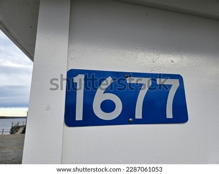 The civic number 1677 attached to a white wall.