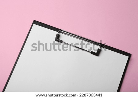 Black clipboard with sheet of blank paper on pink background, top view