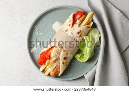 Delicious pita wrap with sausage, french fries and vegetables on light gray table, top view