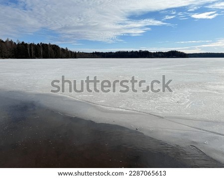Lake landscape on a sunny spring day. The lake's ice has started to melt as the spring sun warms up. The picture shows snow-covered lake and a forest on the horizon. Photographed in Finland.