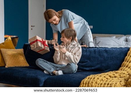 Young woman loving mother surprising son with birthday gift at home, mom giving wrapped box to excited little boy, congratulating child. Overjoyed happy kid sitting on sofa getting present from mum Royalty-Free Stock Photo #2287069653