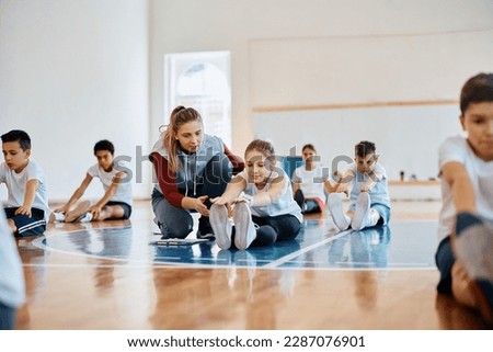 Young physical education teacher assisting kids during exercise class at school gymnasium. Royalty-Free Stock Photo #2287076901