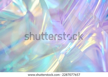 Close-up of ethereal pastel neon mint, turquoise, blue, purple, yellow holographic metallic foil background. Abstract modern curved blurred surreal futuristic disco, techno dreamlike backdrop.
