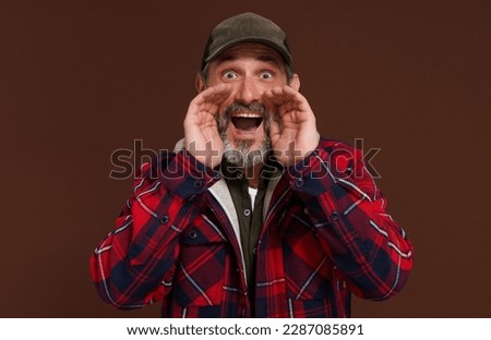 Country style concept. American country man or farmer made megaphone with hands going shout isolated on brown background. High quality photo