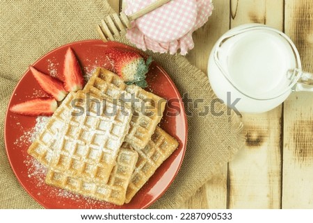 Fresh Belgian waffles with fruits, top view. Tasty breakfast. Homemade waffles with strawberries, powdered sugar on a plate, on a wooden background. Space for text