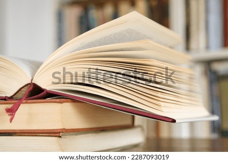 Open book or textbook on a pile of closed books in front of a bookcase in a library. Education learning concept. Image with selective focus. Royalty-Free Stock Photo #2287093019