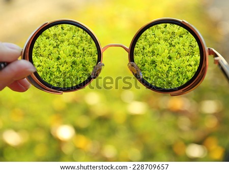 Vision concept. Glasses in hand on green grass background