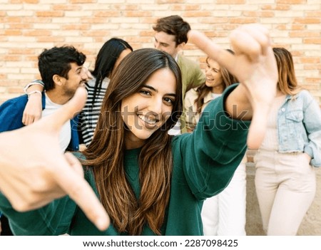 Young adult people having fun together outdoor. Cheerful woman making frame with fingers with multiracial group of friends on the background. Friendship concept