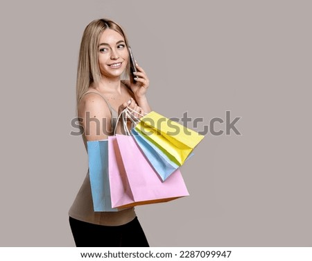 Photo of smiling girl with phone in hand doing shopping isolated on beige background with copy space for text.