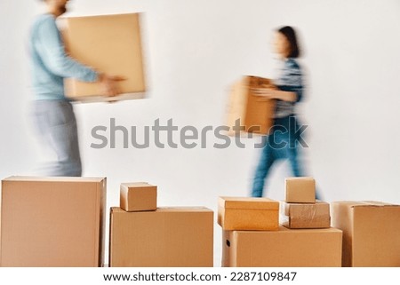 Blurred motion of young couple carrying cardboard boxes moving to new house on white background. Relocation concept