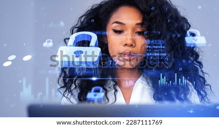 Portrait of young African American businesswoman using laptop in blurry office with double exposure of immersive data protection interface. Concept of cybersecurity