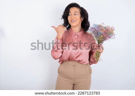 Lovely beautiful woman holding a bouquet of flowers over white background pointing aside with forefinger, showing at copy space having news about bargains