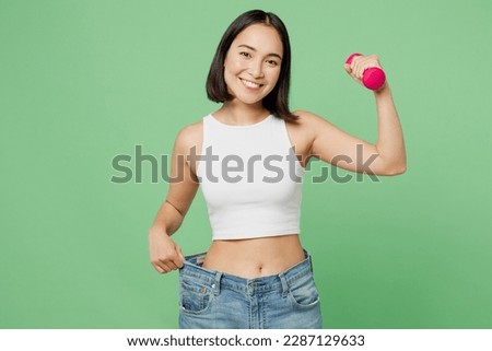Young woman wears white clothes show loose pants on waist after weightloss hold dumbbell isolated on plain pastel light green background. Proper nutrition healthy fast food unhealthy choice concept Royalty-Free Stock Photo #2287129633