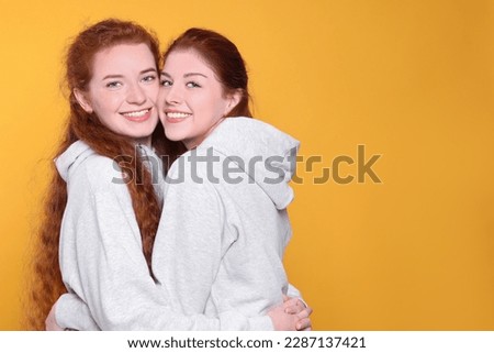 Portrait of beautiful young redhead sisters on orange background. Space for text