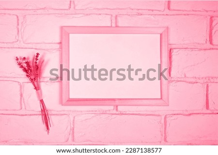 Empty white frame on a background of a white brick wall and a dry bouquet of lavender. Demonstrating the colors of 2023 Viva Magenta.
