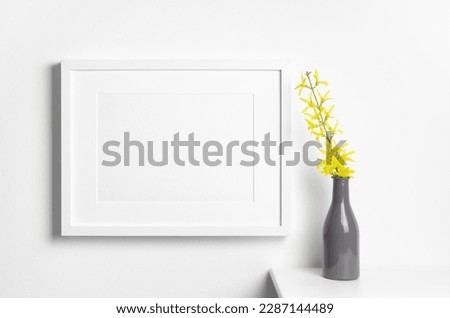 Landscape picture frame mockup on white wall with yellow spring plant decor in vase, blank frame mockup