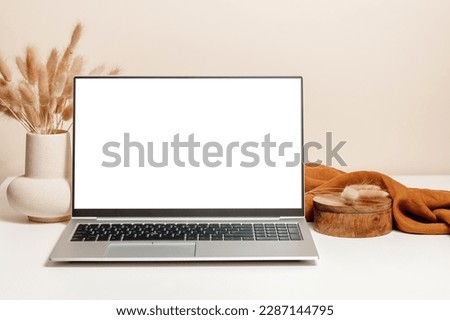 Laptop mockup on the table with ceramic vase, lagurus grass bouquet, wooden box and brown linen cloth with beige wall background. Laptop template for study, home office, website promotion, branding