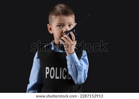 Cute little police officer with radio transmitter on black background