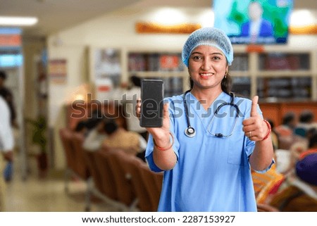 Indian female doctor showing smartphone screen at hospital.