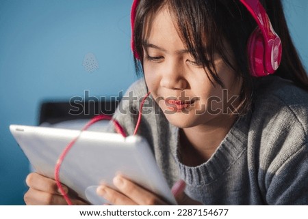 Close up of teenage girl enjoys while listening to music with headphone from tablet computer on her bed.