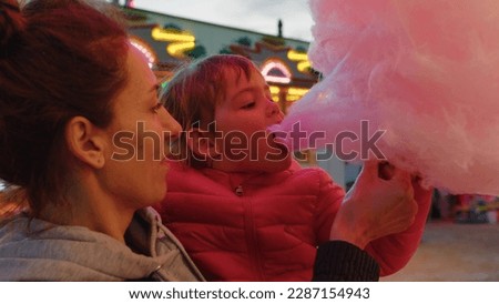 Close up shot of a happy smiling mother and his little daughter are having fun to eat together a cotton candy in amusement park with luna park lights at night Royalty-Free Stock Photo #2287154943
