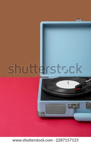 Record player with vinyl disk on table near brown wall