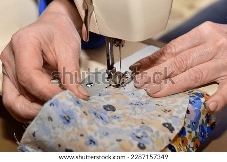 Hands of a seamstress who works on a sewing machine. A seamstress sews two pieces of clothing. Royalty-Free Stock Photo #2287157349