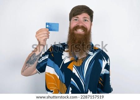 Photo of happy cheerful smiling positive Red haired man wearing printed shirt over white studio background recommend credit card