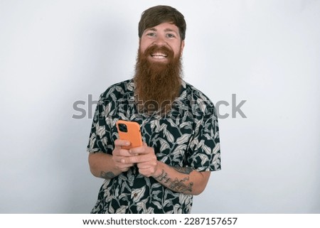 Red haired man wearing printed shirt over white studio background Mock up copy space. Using mobile phone, typing sms message