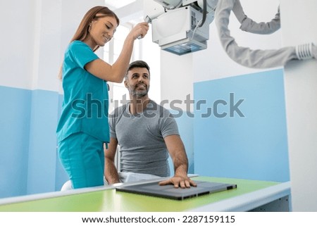 Female radiologist preparing patient for X-ray of hand near X-ray machine. Radiologist Taking X-ray Of Patient Lying On Gurney