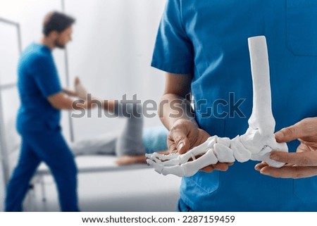 Podiatrist showing anatomical foot skeleton model during his assistant examination injured leg of patient in department of traumatology and orthopedics Royalty-Free Stock Photo #2287159459