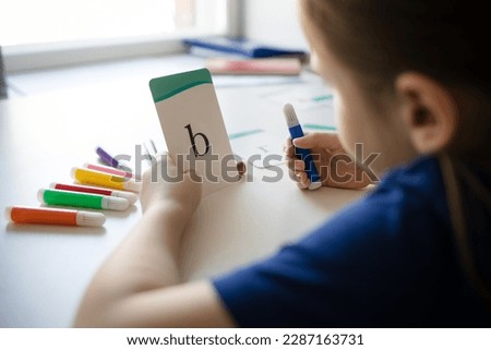 girl holds in her hands card with English letter and felt-tip pen. child learns to read. learning foreign languages at home online