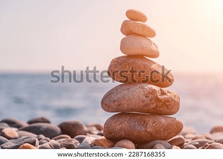 Balanced rock pyramid on sea pebbles beach, sunny day and clear sky at sunset. Golden sea bokeh on background. Selective focus, zen stones on sea beach, meditation, spa, harmony, calm, balance concept