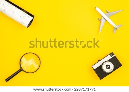 Airplane model, map, camera and magnifier on yellow background, flat lay.