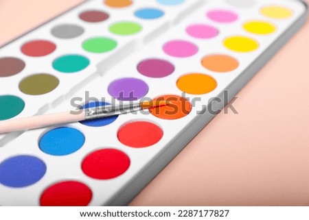 Watercolor palette with brush on beige background, closeup