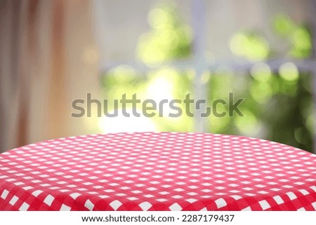 Red and white checkered tablecloth on table near window. Space for design