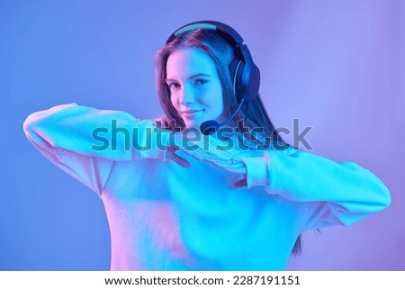 Pretty teenage girl posing in headset and a white hoodie at a studio in mixed color lighting. Modern music. Online communication. Active youth lifestyle. 