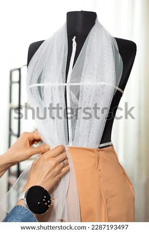 Seamstress tailor works with fabric for sewing designer clothes using a mannequin.
