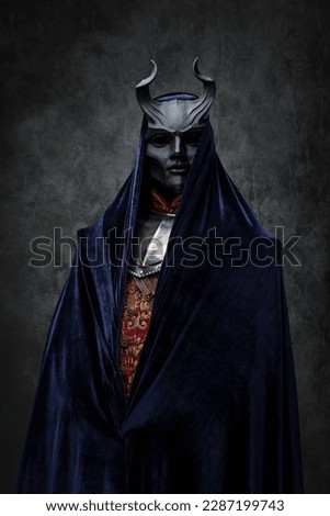 Shot of dark cult prayer dressed in robe and evil mask against dark background. Royalty-Free Stock Photo #2287199743