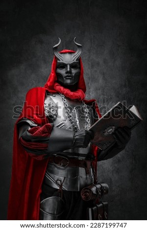 Shot of mysterious cultist dressed in steel armor and red mantle holding book.