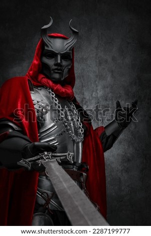 Shot of leader of esoteric cult dressed in silver armor and red mantle with horned mask. Royalty-Free Stock Photo #2287199777