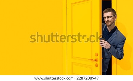 Cheerful, smiling, stylish man in formal wear, businessman peeking out yellow door with coffee. Job fair, employment, education. Concept of emotions, facial expression, lifestyle, work Royalty-Free Stock Photo #2287208949