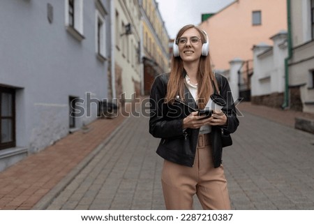 young female freelancer music lover wearing headphones and walking in the city street Royalty-Free Stock Photo #2287210387