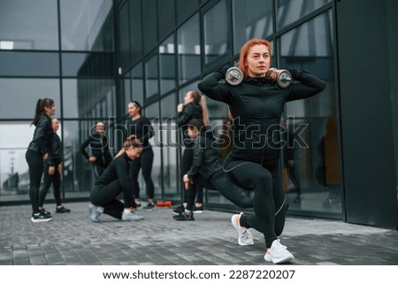 Beautiful woman is standing in front of her friends. Group of sportive women is outdoors near black building.