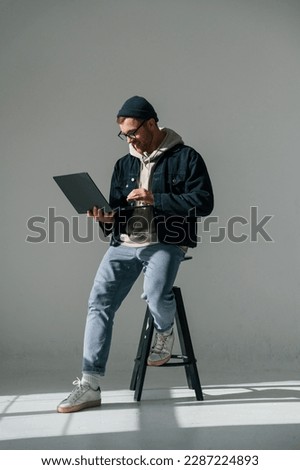 Sitting on the chair and holding laptop. Handsome man is in the studio against white background.