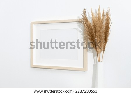 Wooden artwork frame mockup on white wall with dry grass decoration, horizontal mockup with copy space