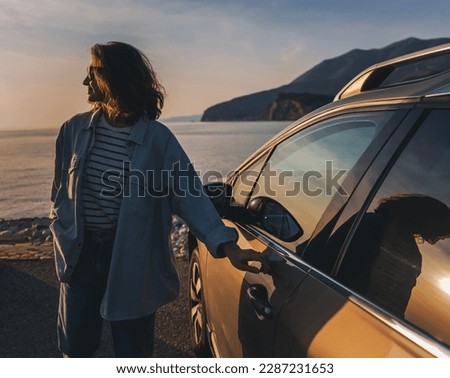 Young happy woman traveler opening car door. Sunset beach portrait Royalty-Free Stock Photo #2287231653